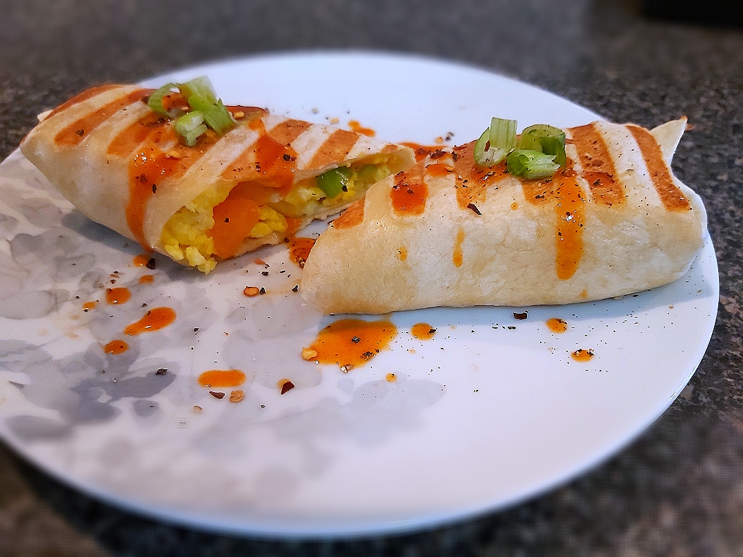 BentoFox's dish Scrambled eggs, red & orange bell peppers, chives and grated marble cheese in a lightly grilled wrap topped with a spicy Cholula sauce and black pepper 👌